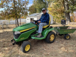 Man on John Deere Tractor with small cart behind to haul wood.