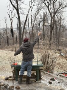 Man reaches with stick to break ice off suet feeder.