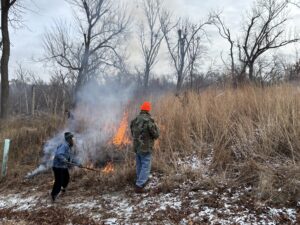 Two people watch over the prairie burn