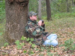 Man sits at tree base with binoculars.