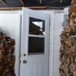 Cord wood stacked out of the weather near a door.