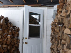 Cord wood stacked out of the weather near a door.