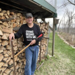 Man stands by wood pile.