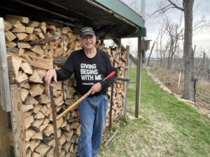 Man stands by wood pile.