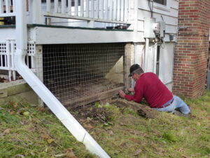 Man fixes wire on porch sides to prevent woodchucks from living underneath the porch.