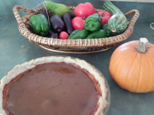Pumpkin pie, small pie pumpkin, and basket of peppers & tomatoes on countertop.